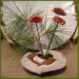rusty mums and white pine in a cream ceramic vase