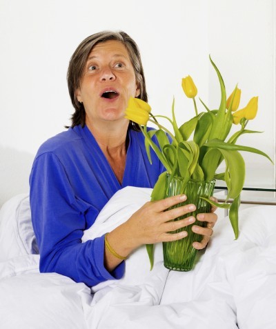woman in her fifties sitting in bed and holding a vase with flowers